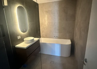 Freestanding bath with stone-look tiles, floating vanity and backlit mirror at Palm Beach