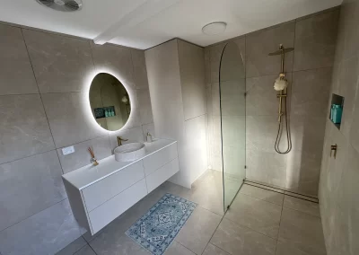 Completed bathroom with floating vanity, round LED mirror and brass shower fixtures at Main Beach