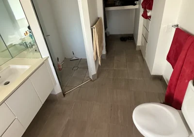 Narrow bathroom with dated vanity, mirror and tile flooring before renovation at Palm Beach