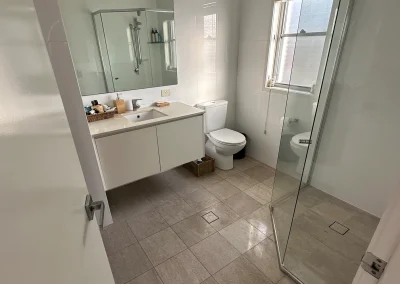 Glass shower screen, white vanity and grey tiles in the Palm Beach bathroom before renovation