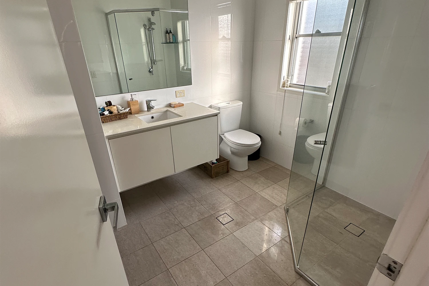 Glass shower screen, white vanity and grey tiles in the Palm Beach bathroom before renovation