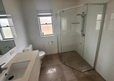 Small bathroom with corner shower, louvre window and worn fittings before renovation at Palm Beach
