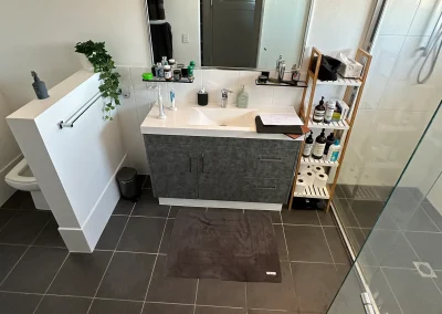 Dated bathroom with dark floor tiles, white vanity and bamboo shelf before refit at Palm Beach