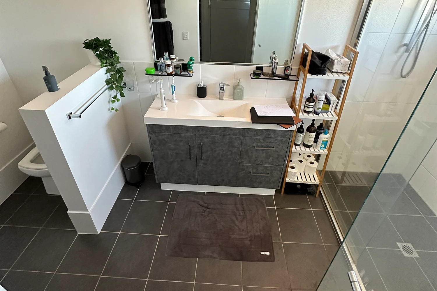 Dated bathroom with dark floor tiles, white vanity and bamboo shelf before refit at Palm Beach
