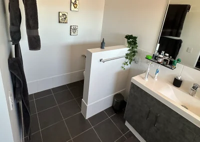 Cluttered vanity area with towel rail and dark tiles before bathroom refit at Palm Beach