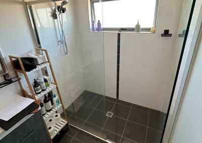 Old shower with glass screen, dark floor tiles and window shelf before refit at Palm Beach