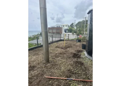 Bare dirt yard with exposed pipes and steel post before deck build in Currumbin